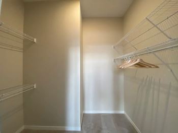 A walk-in closet with white shelves and a light brown hanging rod.